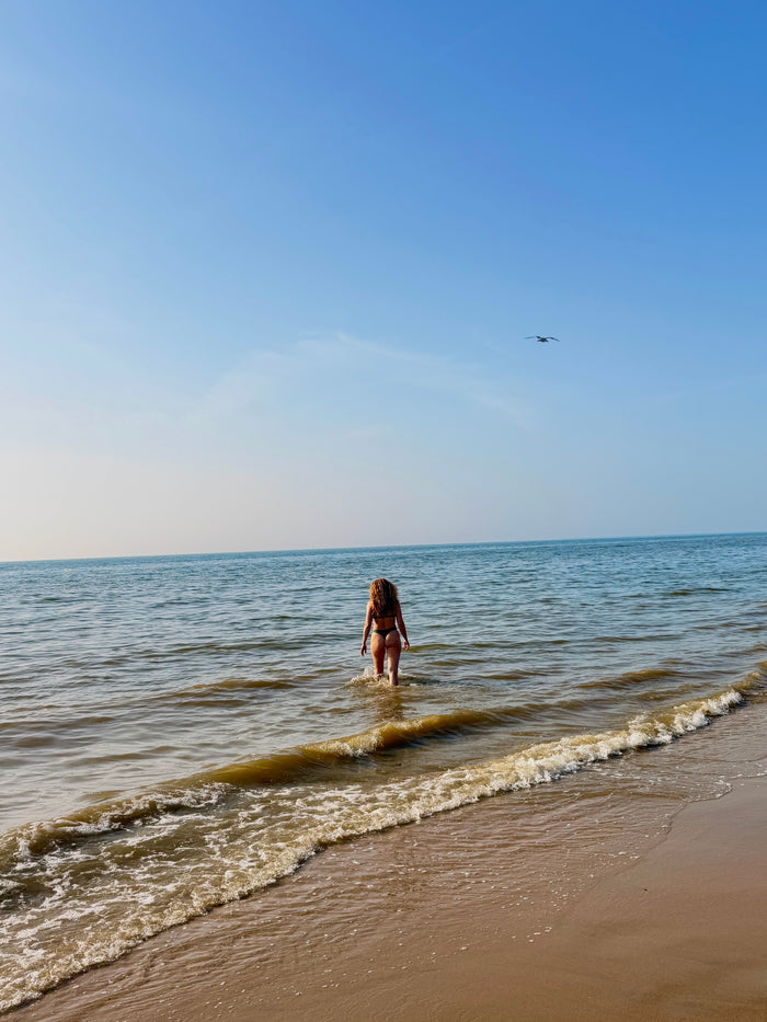 model met krullen lopend in de zee in groene bikini