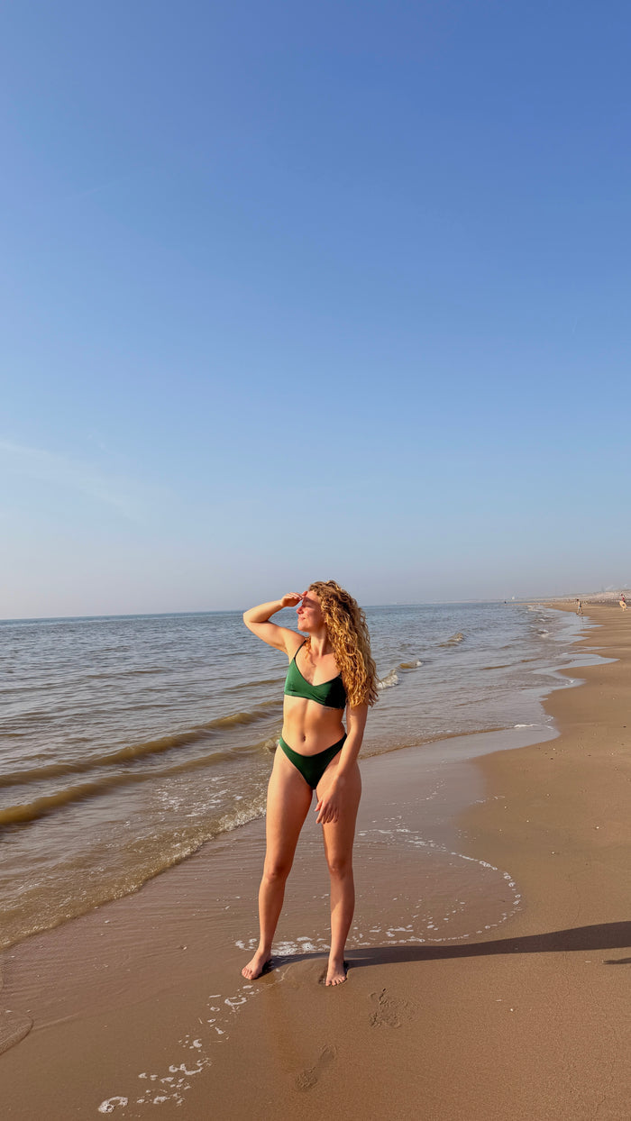 model in groene bralette bikini van pavo couture poserend op strand
