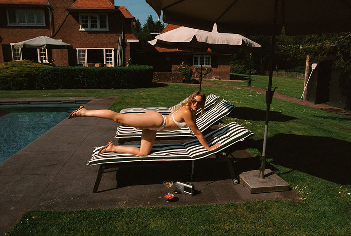 geraldine kemper met gestreekt been geposeerd op ligbedje bij zwembad in witte lingerie