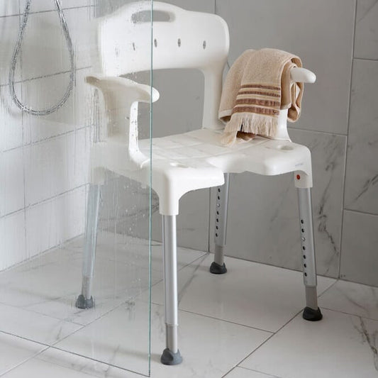 Angled view of Etac Swift Shower Chair with Arm Supports with moulded seat, supportive backrest and height-adjustable legs on a plain background.