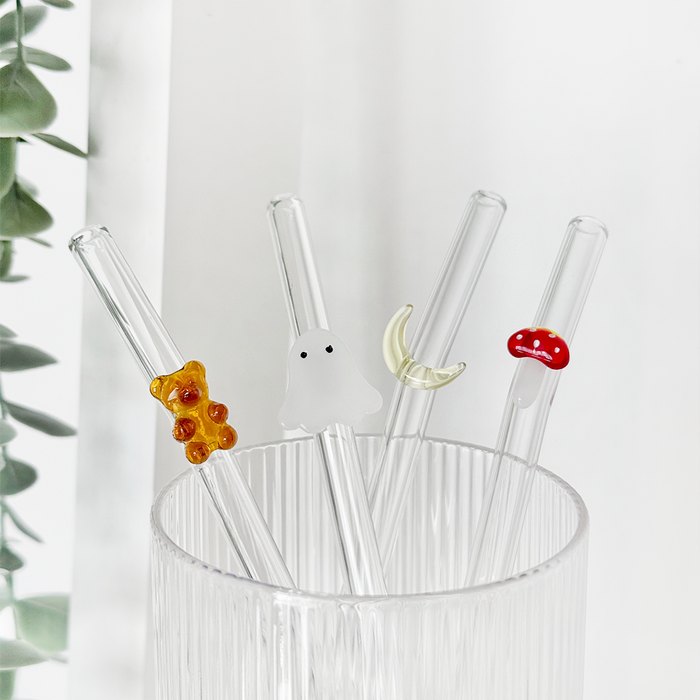 Set of four glass straws with autumn-themed designs in a clear ribbed glass cup.