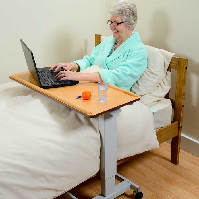 Side view of NRS Easylift Overbed Table showing the tilting top and height-adjustable chrome stems.