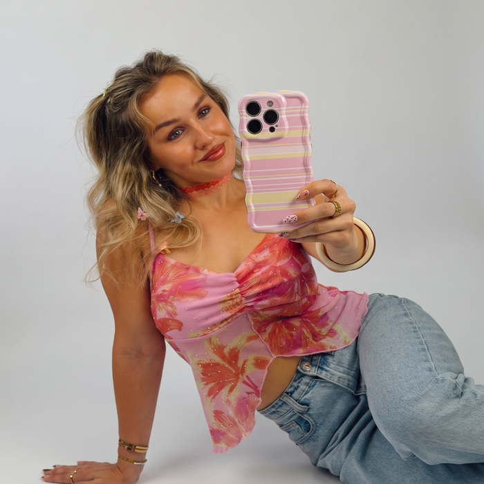Woman taking a selfie, holding an iphone in a pink, white and yellow horizontal striped wavy phone case.